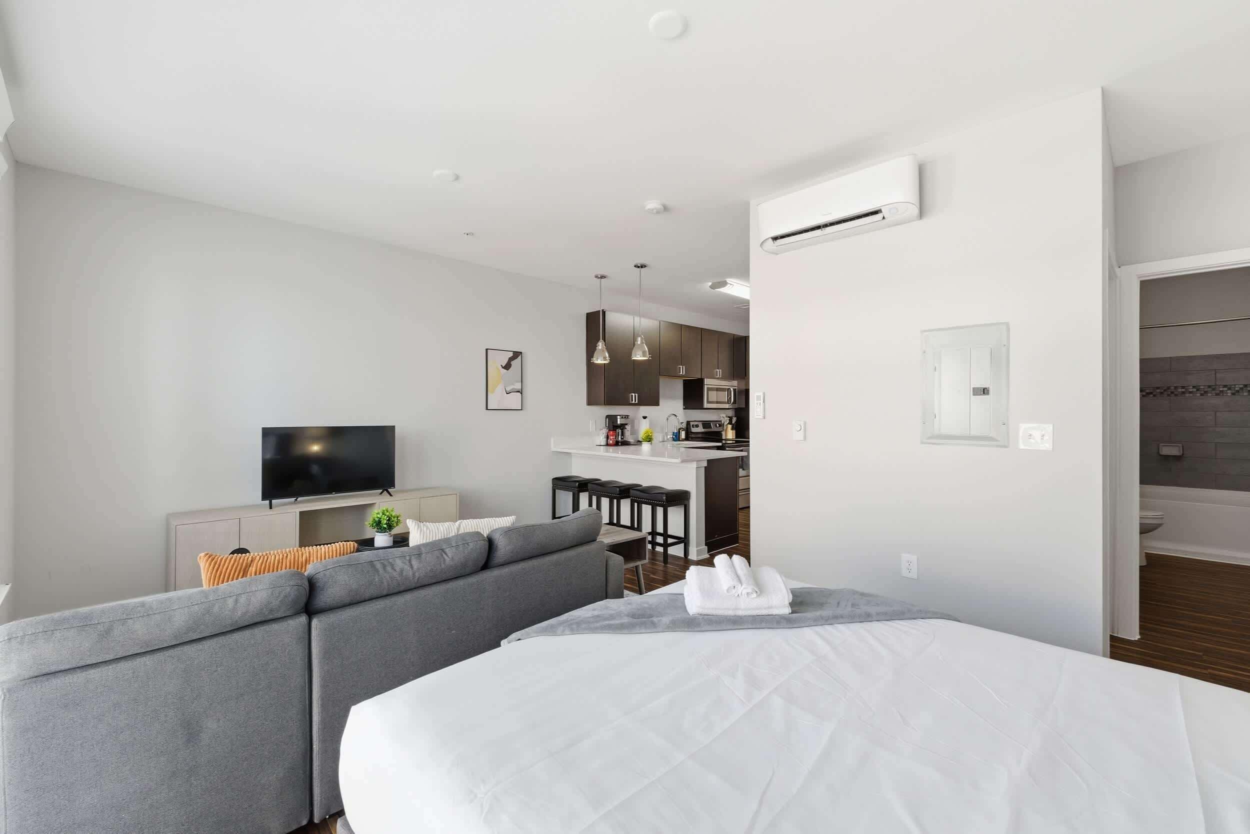 Una habitación de hotel moderna con una cama grande, un sofá, un televisor, una kitchenette y un baño.