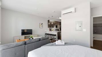 Una habitación de hotel moderna con una cama grande, un sofá, un televisor, una kitchenette y un baño.