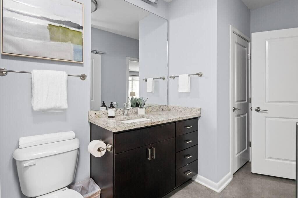 Un baño con inodoro, mueble de madera oscura, encimera, lavabo y espejo.