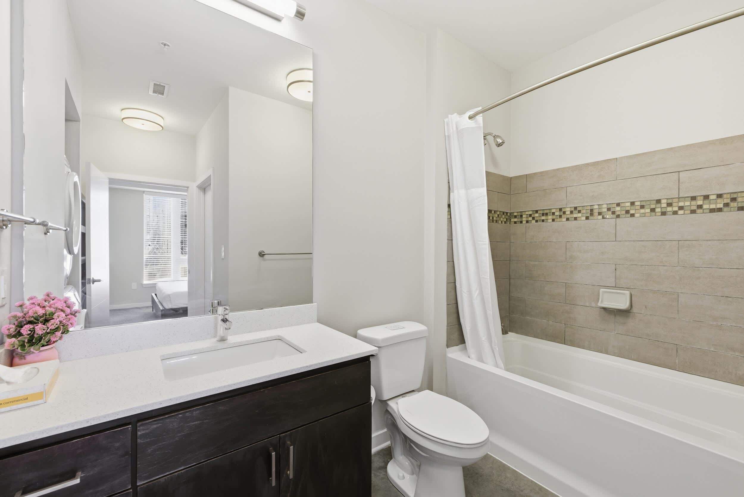 Un baño moderno con un lavamanos blanco, armarios oscuros, un inodoro y una bañera con cortina de ducha.
