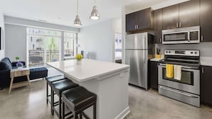 A modern kitchen with stainless steel appliances, a central island with bar stools, and pendant lighting. - CozySuites at Artistry Indy (Indianapolis)