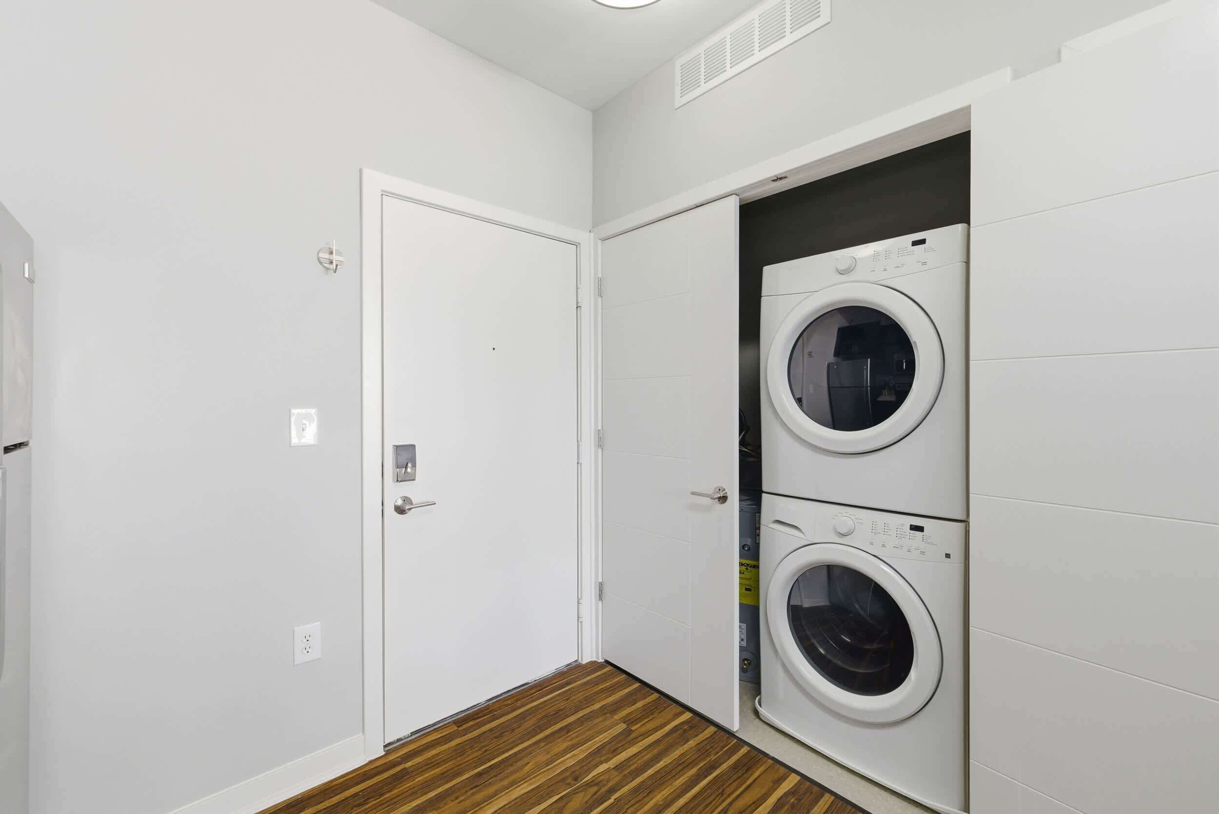Un cuarto de lavandería con dos lavadoras apiladas y una puerta que da a otra habitación.