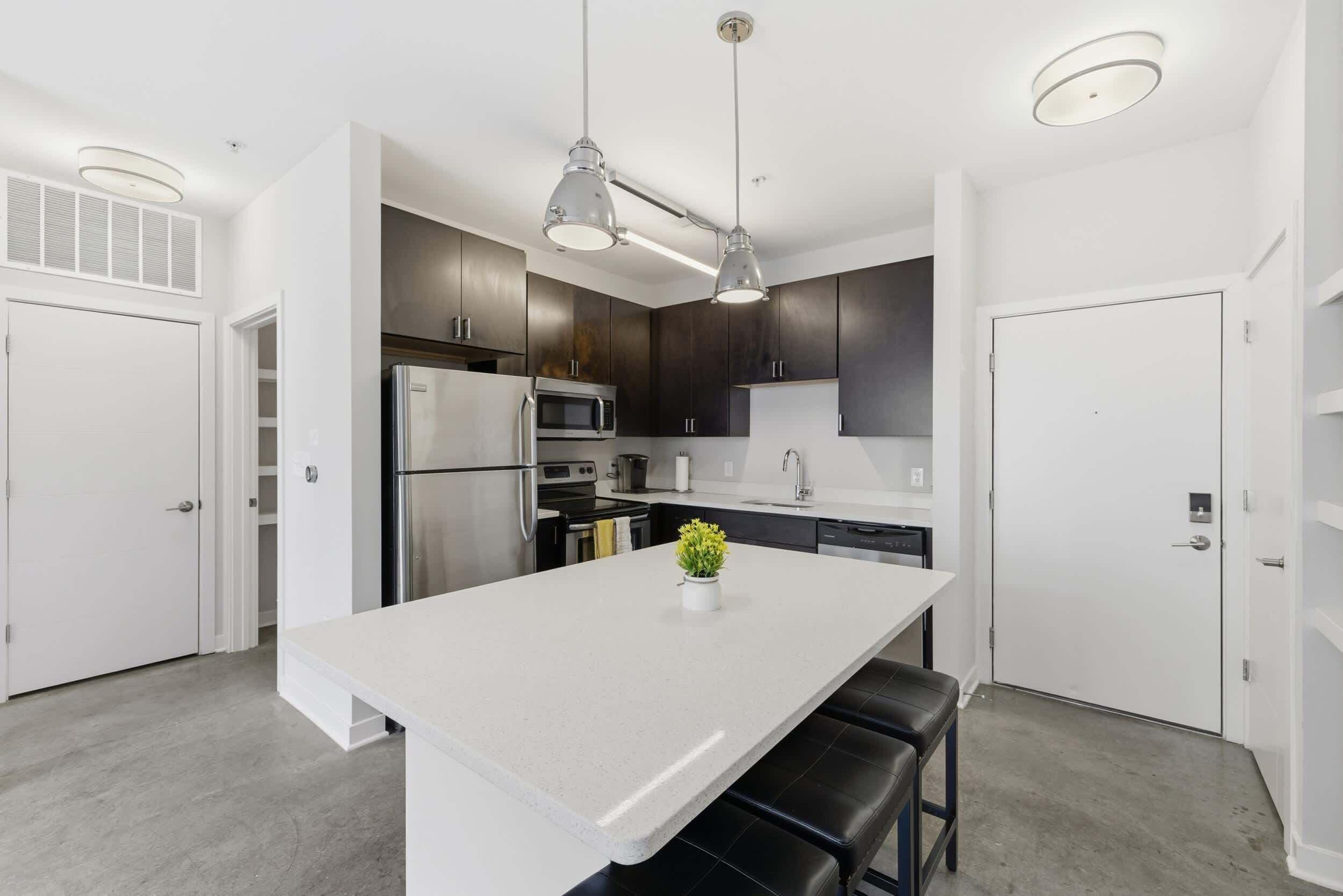 Une cuisine moderne dotée d’un îlot central, d’appareils électroménagers en acier inoxydable et de luminaires suspendus.