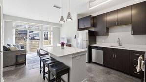 A modern kitchen with dark cabinets, a white island, stainless steel appliances, and pendant lighting. - CozySuites at Artistry Indy (Indianapolis)