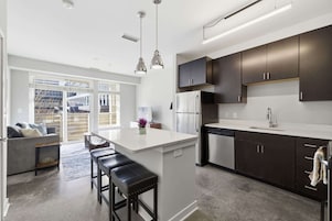 Una cocina moderna con armarios oscuros, una isla blanca, electrodomésticos de acero inoxidable e iluminación colgante.