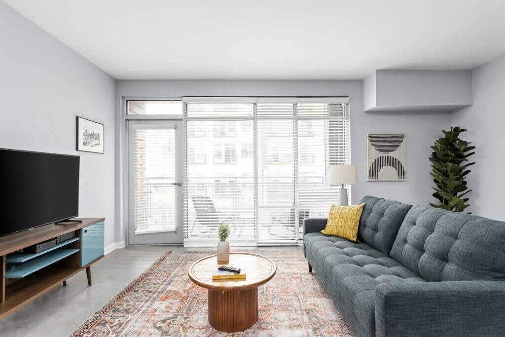A modern living room with a grey sofa, a coffee table, a TV on a wooden stand, and a patterned rug.