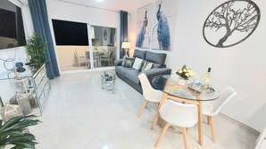 Een moderne woonkamer met een grijze bank, witte stoelen, een glazen salontafel en een eethoek met een dienblad vol drankjes.