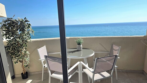 Een balkon met een tafel, stoelen, een potplant en uitzicht op zee.