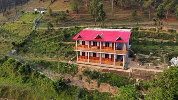A two-story building with a red roof, surrounded by lush greenery and hills.