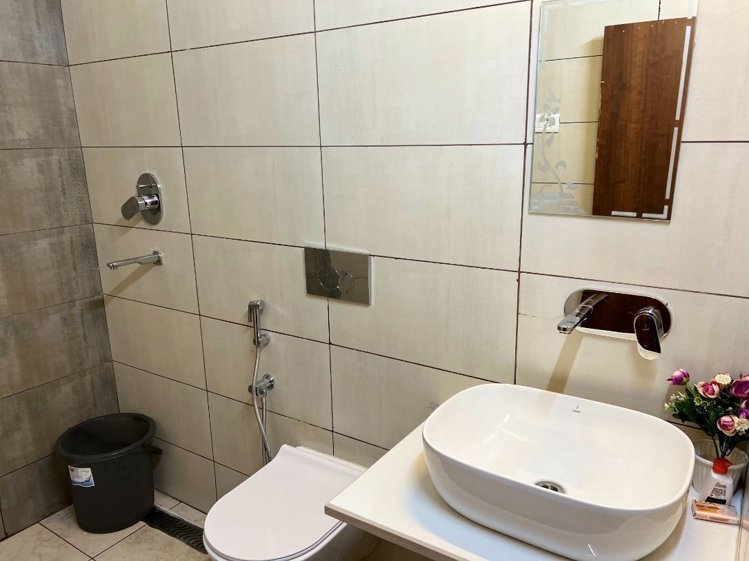 A bathroom with a toilet, sink, shower, and a trash bin.