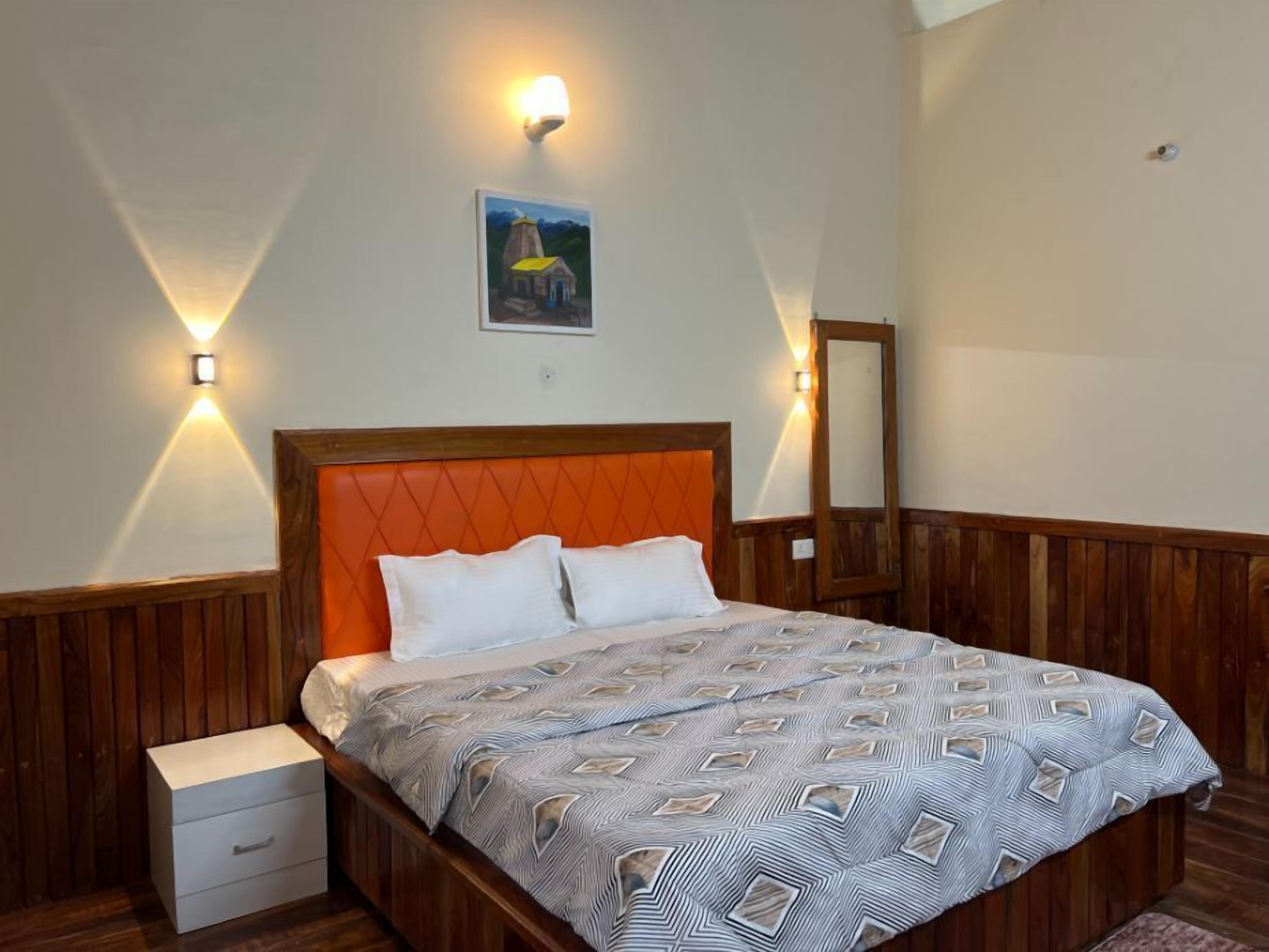 Une chambre à coucher avec une tête de lit en bois, deux tables de chevet, un lit avec une literie à motifs et deux lampes fixées au mur.