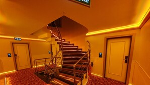 A hotel hallway with a spiral staircase, carpeted floors, and doors with electronic keycard readers.