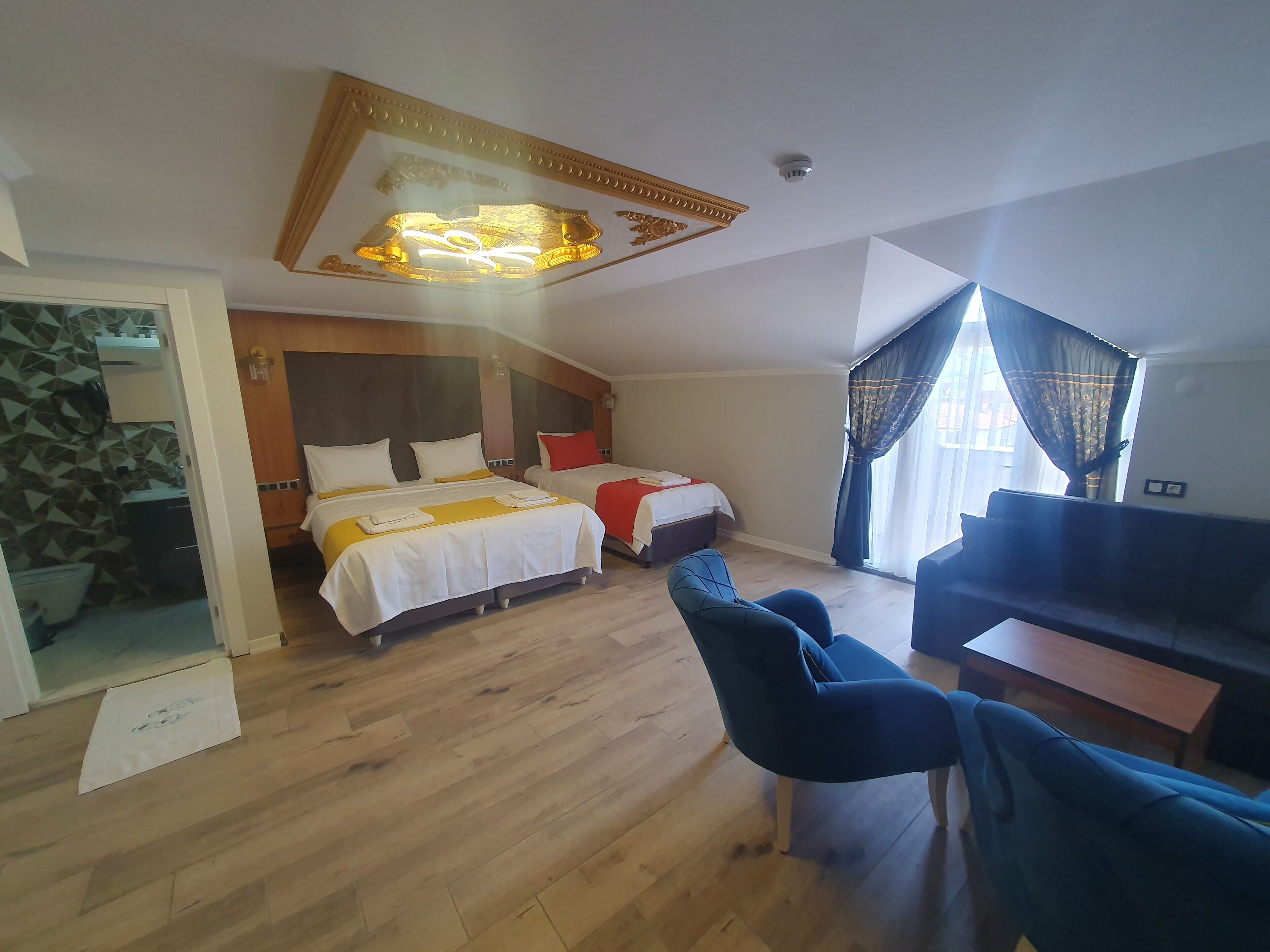 A hotel room with two beds, a sofa, a desk, and a bathroom visible through an open door.