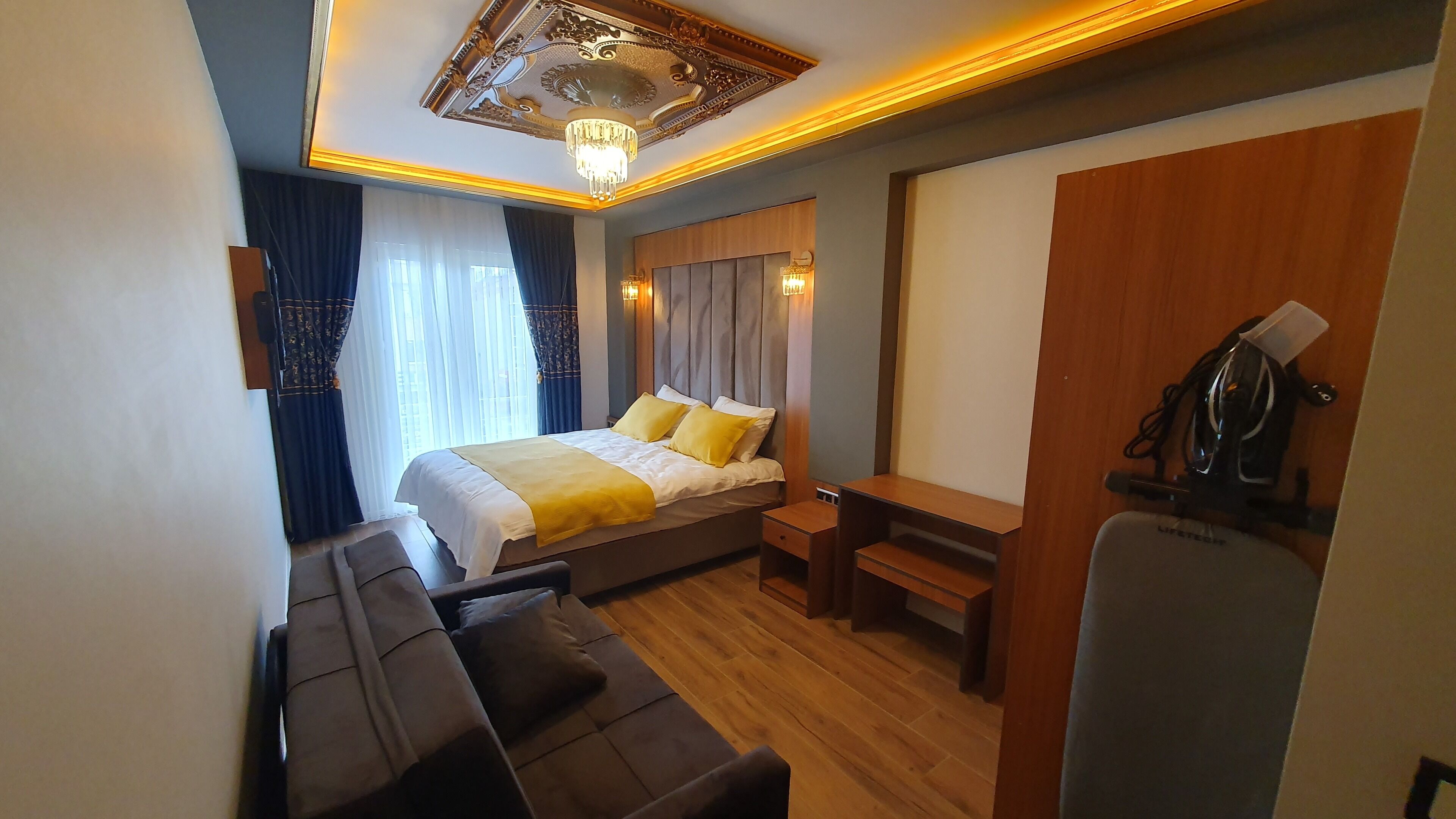 A hotel room with a bed, a desk, a chair, a sofa, and a ceiling light fixture.