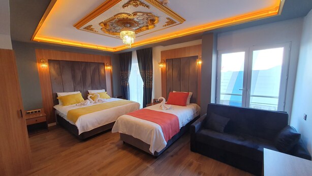 A hotel room with two beds, a sofa, a chandelier, and a large window.
