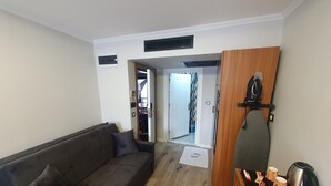 A living room with a dark grey sofa, a wooden table with a kettle and cups, and a door leading to a bathroom.