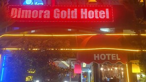 The exterior of the Dimitrova Gold Hotel with a prominent illuminated sign, flags, and a well-lit entrance area.