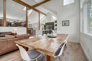 A spacious dining area with a large wooden table, white chairs, and a view of the kitchen and living area. - Chateau Nouveau TRUE Ski-in/out / EPIC Views - Access to Peak 8, Hot Tub & More (Breckenridge)