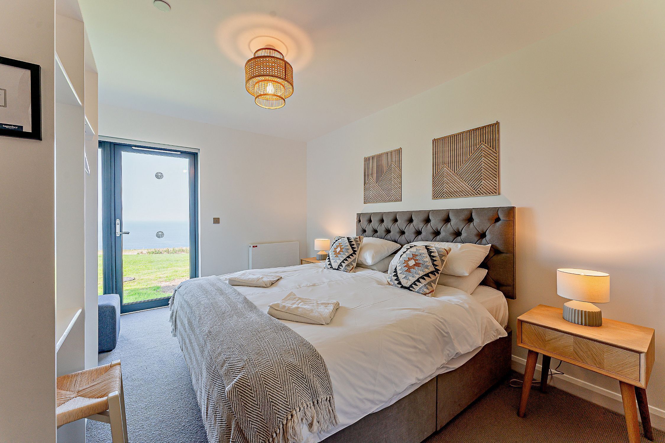 A bedroom with a large bed, a bedside table with a lamp, a chair, and a view through an open door.