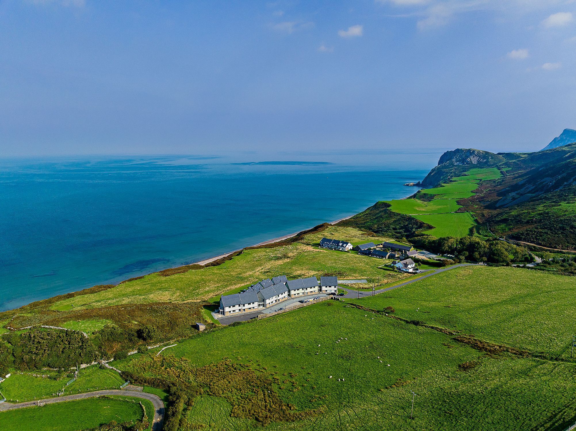 A coastal property with a large house and several smaller buildings, surrounded by green fields and a view of the sea.