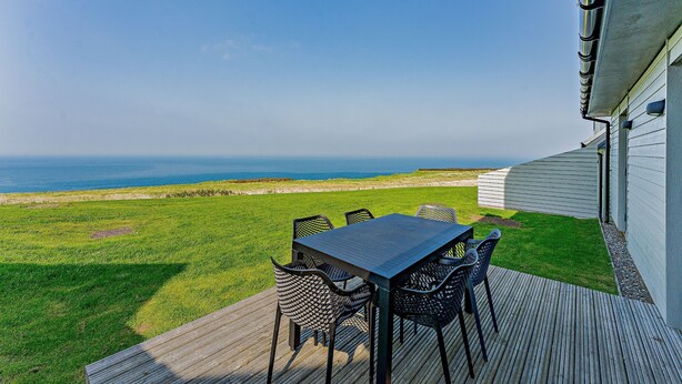 A deck with a table and chairs overlooking a grassy area and the ocean. - Cosy, 3-bedroom cottages with uninterrupted views of the sparkling Llyn Peninsula coastline. (Pwllheli)