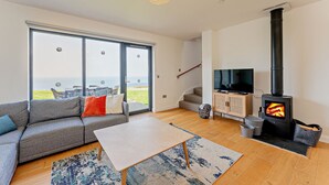 A modern living room with a sofa, a coffee table, a fireplace, and a TV. - Cosy, 3-bedroom cottages with uninterrupted views of the sparkling Llyn Peninsula coastline. (Pwllheli)