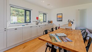 A modern kitchen with white cabinets, a wooden dining table, and a view of greenery outside. - Cosy, 3-bedroom cottages with uninterrupted views of the sparkling Llyn Peninsula coastline. (Pwllheli)