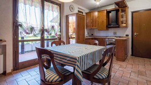 A dining area with a table and chairs, wooden cabinets, a stove, and a door. - Holiday apartment near the center with swimming pool, air conditioning, parking lot (Lazise)