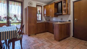A kitchen with wooden cabinets, a gas stove, and a dining table with chairs. - Holiday apartment near the center with swimming pool, air conditioning, parking lot (Lazise)