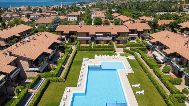 A resort with a central swimming pool, multiple villas, and a mountainous backdrop. - Holiday apartment near the center with swimming pool, air conditioning, parking lot (Lazise)
