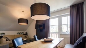 Una sala de estar moderna con una mesa de comedor de madera, sillas de cuero negro, un sofá y un televisor montado en la pared.
