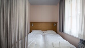 Un lit double avec du linge de lit et des serviettes blanches, une tête de lit en bois et une table de chevet avec une lampe.