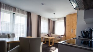 A modern living room with a sofa, a dining table, and a kitchen area with a sink and coffee maker.