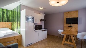 Une pièce compacte comprenant un lit, une kitchenette, un coin repas et un téléviseur fixé sur un panneau en bois.