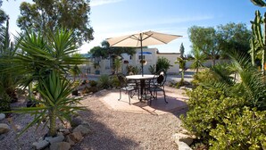 An outdoor patio with a table and chairs, surrounded by various plants and a large umbrella. - La Casita mit Pool (Valle del Sol)