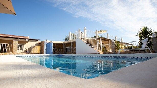 A swimming pool with a clear blue sky, a white building with a red roof, and a staircase leading to a covered area. - La Casita mit Pool (Valle del Sol)