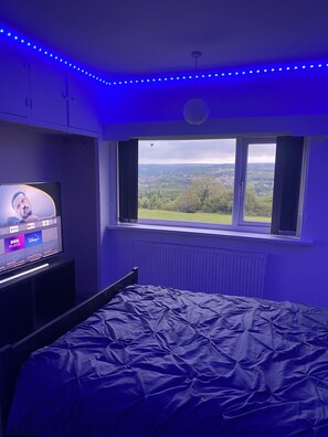 Une chambre à coucher avec un lit, un téléviseur diffusant des services de streaming et une fenêtre donnant sur un paysage verdoyant.