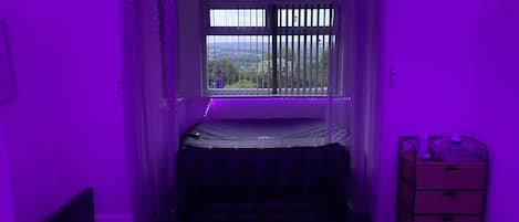 A room with a bed, a window with bars, a small table with items, and a curtain.