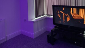 Una habitación con ventana, radiador y televisor sobre un soporte.