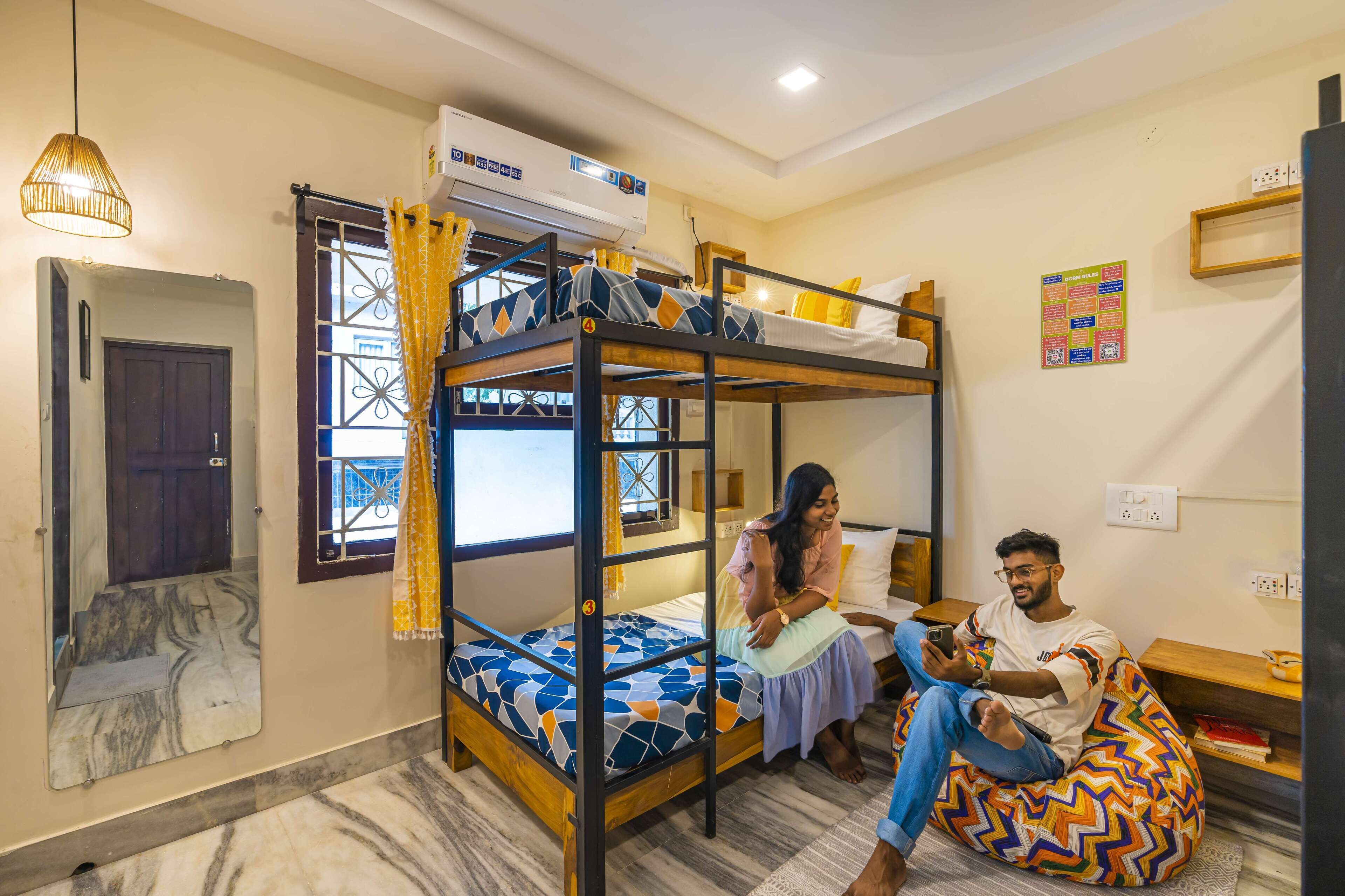 Habitación con literas, un espejo, ventana con cortinas, mesita de noche y aire acondicionado de pared.