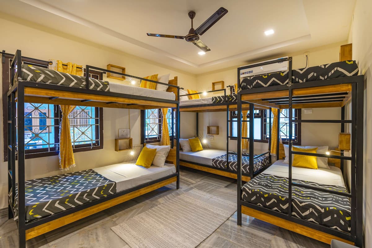 Ein Zimmer mit drei Etagenbetten, jeweils mit einem gemusterten Bettbezug, einem Deckenventilator und einem Vorhangfenster.