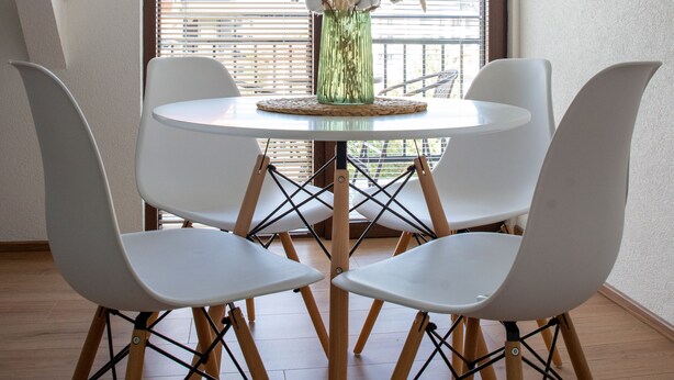 A dining area with a round table, four white chairs, and a green vase with dried plants. - Daria Apartment (Ohrid)
