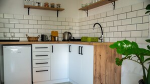 A kitchen with white cabinets, a dishwasher, and wooden shelves above. - Daria Apartment (Ohrid)