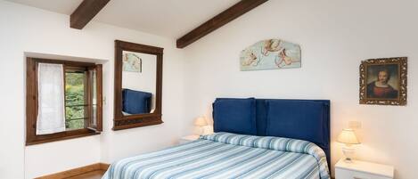 A bedroom with a bed, a nightstand, a lamp, a window with curtains, a mirror, and wall art.
