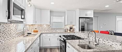 A modern kitchen with white cabinets, a granite countertop, a built-in oven, and a stainless steel refrigerator.
