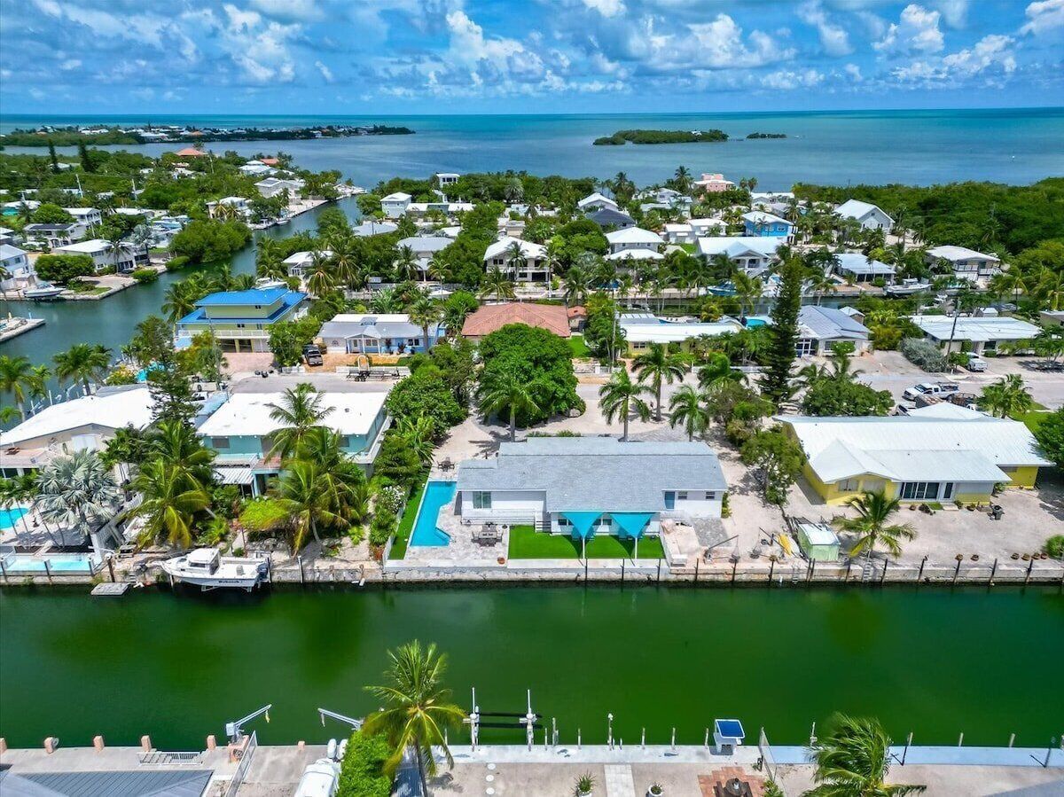 An aerial view of a coastal residential area with houses, a marina, and a clear view of the ocean.