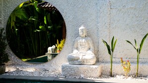Un entorno exterior tranquilo con una estatua de Buda, un estanque circular y abundante vegetación.