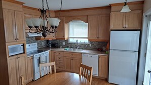 A kitchen with wooden cabinets, a white refrigerator, a microwave, a stove, and a dining table with chairs. - Very nice little condo for rent (Saguenay)