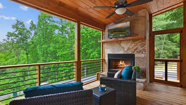 Una terraza de madera con mobiliario de mimbre, chimenea y vistas panorámicas a árboles.
