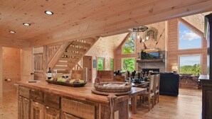 Interior espacioso de una cabaña de madera con una amplia cocina, una mesa de comedor y una chimenea.
